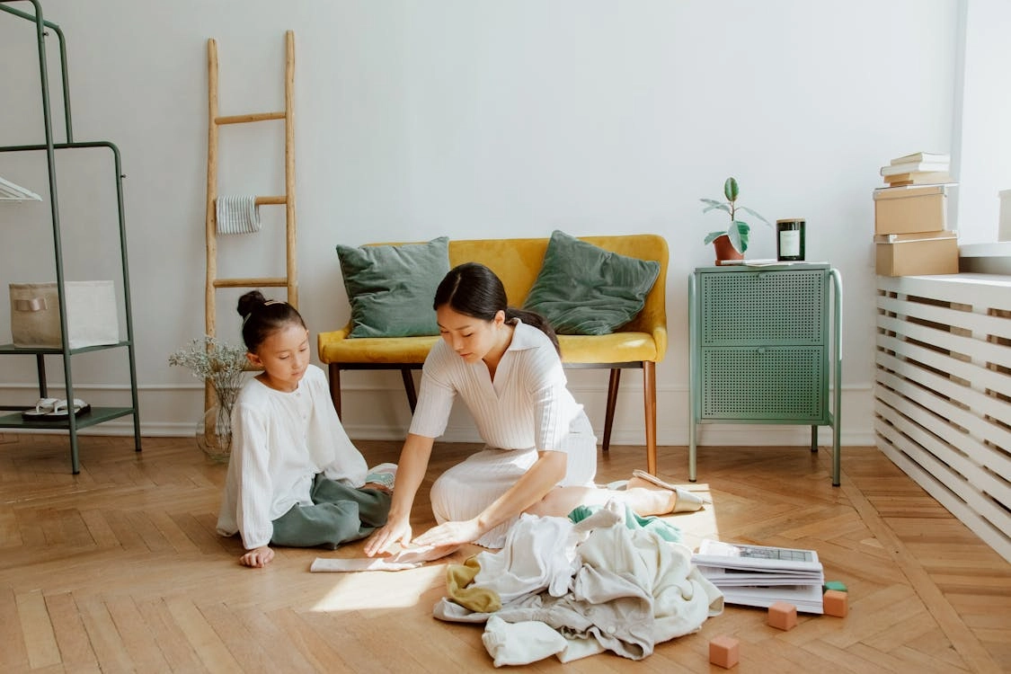 Caregiver and girl folding clothes together in cozy living room, promoting bonding and early learning.
