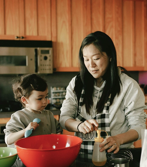 Caregiver and Toddler cooking together in kitchen, mixing ingredients and nurturing shared moments.