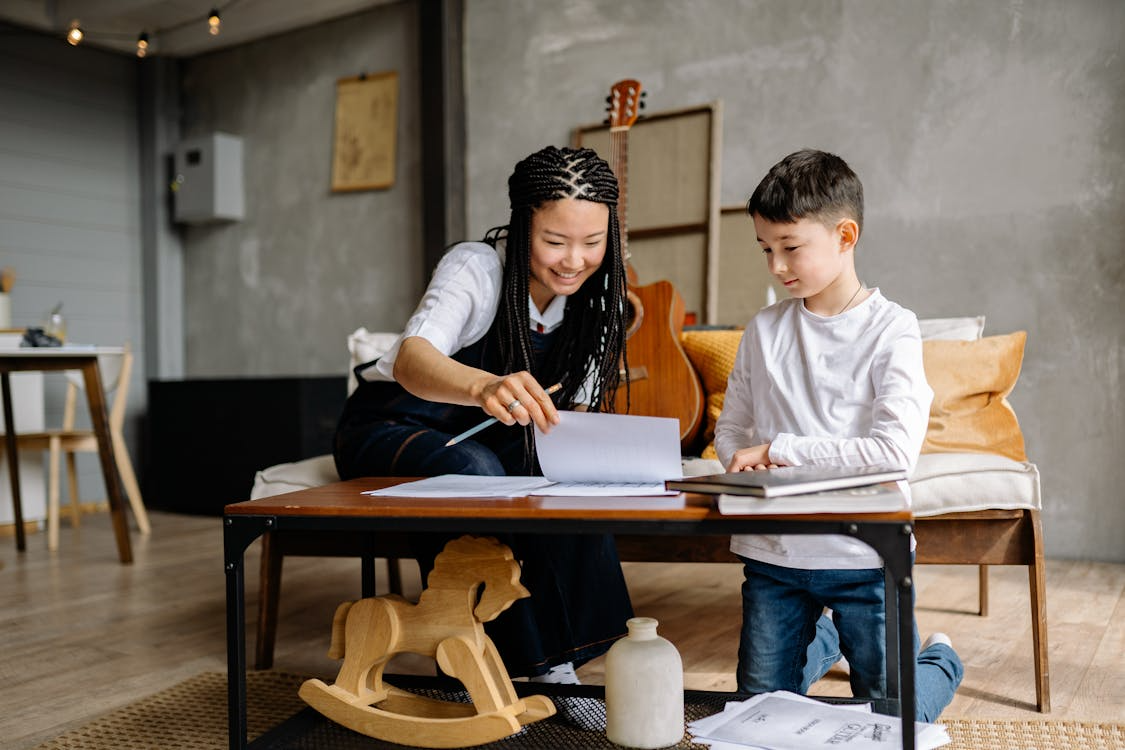 Woman assisting child with project at table in warm home setting, encouraging learning.