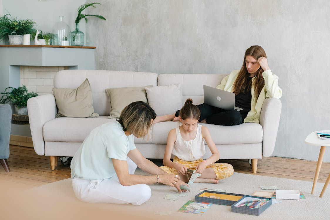 Nanny and child drawing on the floor, while mother doing work on sofa, fostering creativity and bonding.
