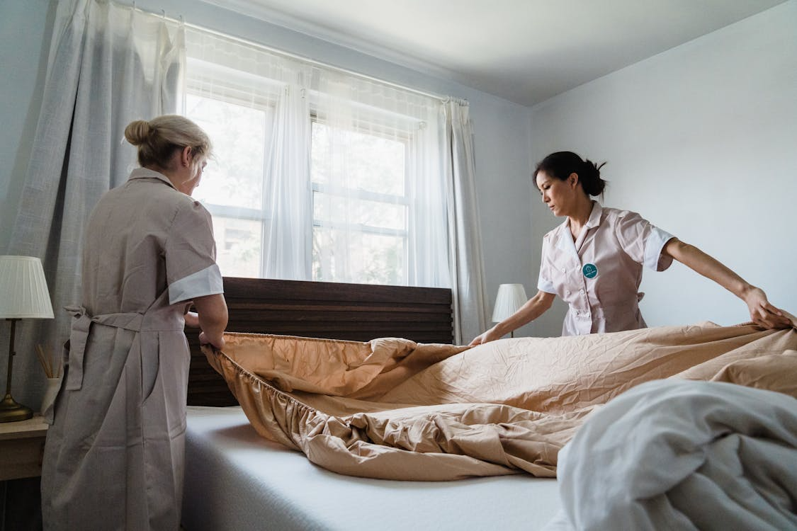 Housekeepers making bed and tidying bedroom, creating clean and welcoming home setting.