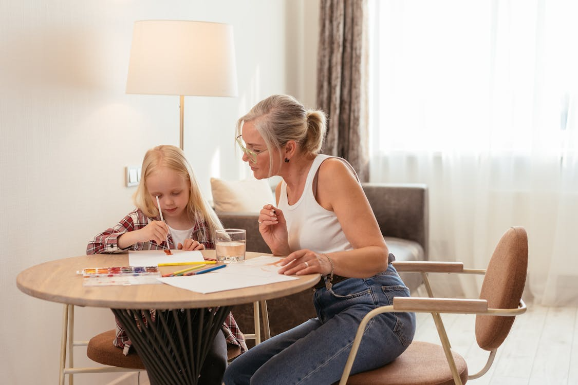Woman guiding child with writing at table, focused learning environment and educational support.
