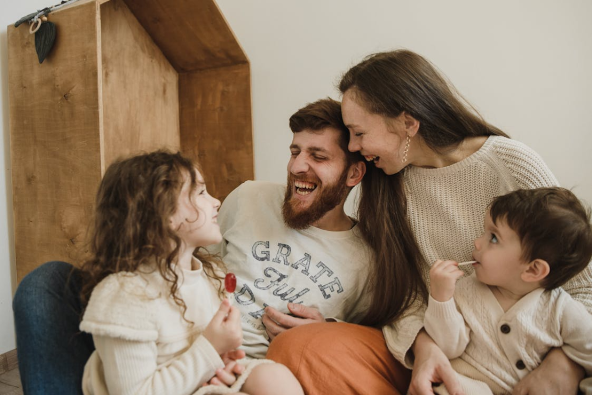 Family sitting together in living room, parents and children sharing laughter and emotional warmth.