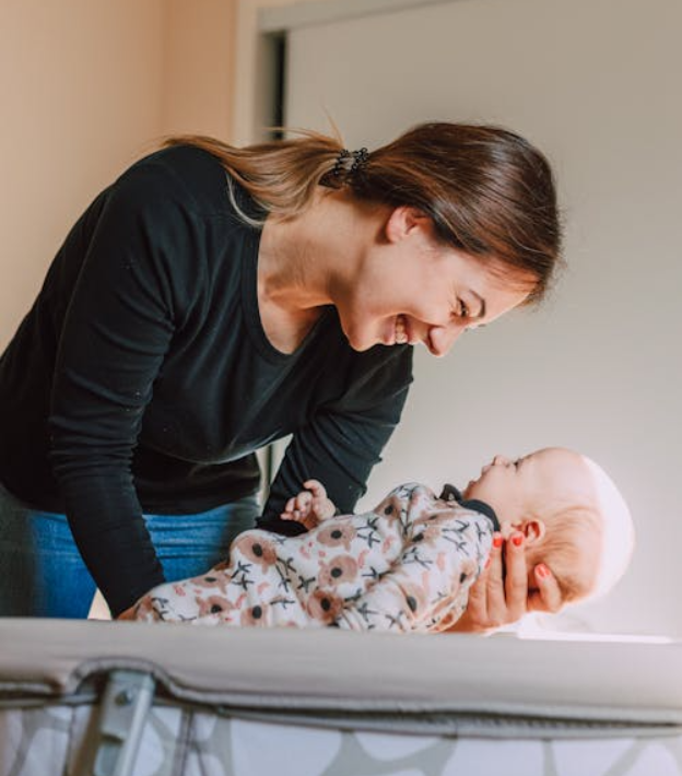 Woman leaning over crib, smiling at baby, celebrating bond and nurturing care.
